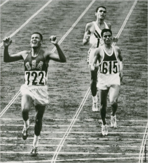 Billy Mills crossing finish line with two other runners close behind ...