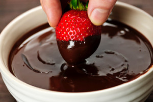 Hand dipping fresh strawberry in melted chocolate