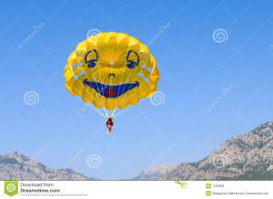 Smiling funny parachute in blue sky over mountains.