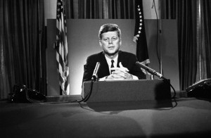 President John F. Kennedy sits behind microphones at his desk in ...
