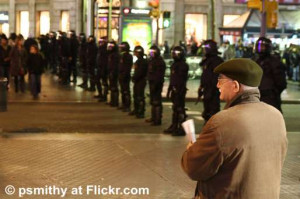 Elderly Man Looking At A Line Of Riot Police