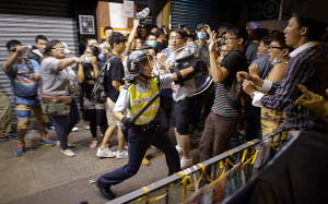 policeman holding a baton advances towards pro-democracy protesters ...