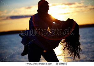 Silhouettes of happy guy holding his girlfriend by the lake at sunset