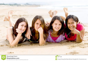 Four teenage girls lying on the beach together smiling.