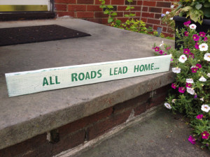 Small wood sign with the quote “All Roads Lead Home”