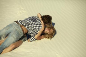 Young couple lying in the sand hugging each other - Justin Case ...