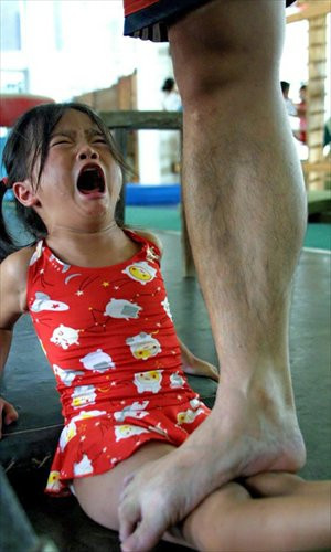 girl cries as a coach stands on her legs to help stretch her ...