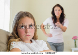Angry little girl with mother scolding her in background at home ...