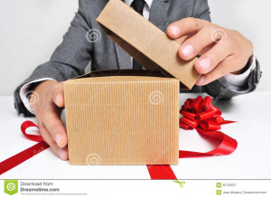 ... wearing a suit sitting in a table opening a gift with a red ribbon
