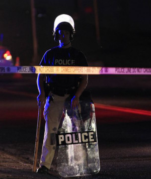 policeman wearing riot gear tries to disperse a crowd in Ferguson ...