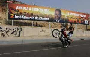 motorcyclist rides past an election poster of the ruling MPLA party ...