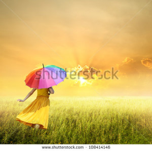 Beautiful woman holding multicolored umbrella in green grass field and ...