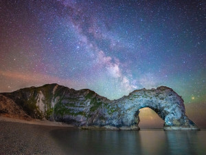 The Milky Way seen behind the natural archway of Durdle Door in a shot ...