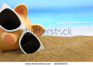 Summer piggy bank with sunglasses on the beach - stock photo
