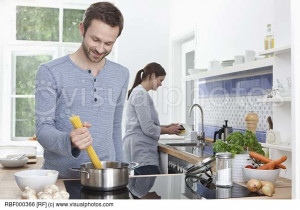 Germany, Bavaria, Munich, Man cooking spaghetti in kitchen, woman in ...