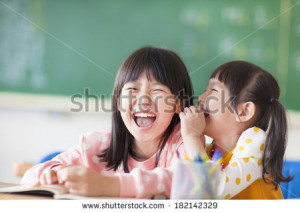 Laughing little girls sharing secrets in class - stock photo