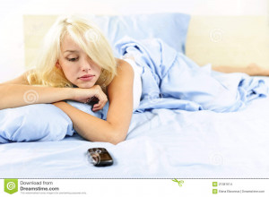 Sad blonde woman waiting for phone call in bed at home.