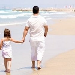 Girl holding daddy's hand while walking on the beach