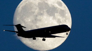PHOTO: An airplane passes a nearly full moon as it makes its approach ...
