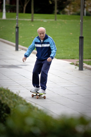 An elderly man riding a skateboard in a tracksuit and looking very ...