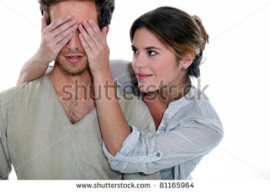 Young woman holding her hands over a man's eyes - stock photo