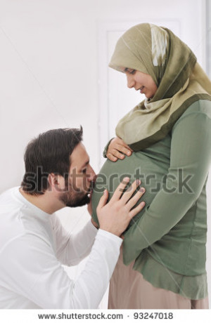 Pregnant muslim wife smiling with her husband kissing belly,and his
