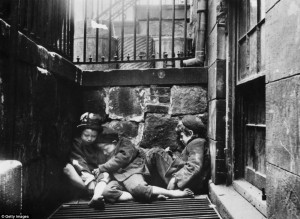 Three children huddle together over a grate for warmth in an alleyway ...