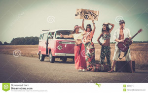 Multi-ethnic hippie hitchhikers with guitar and luggage on a road.